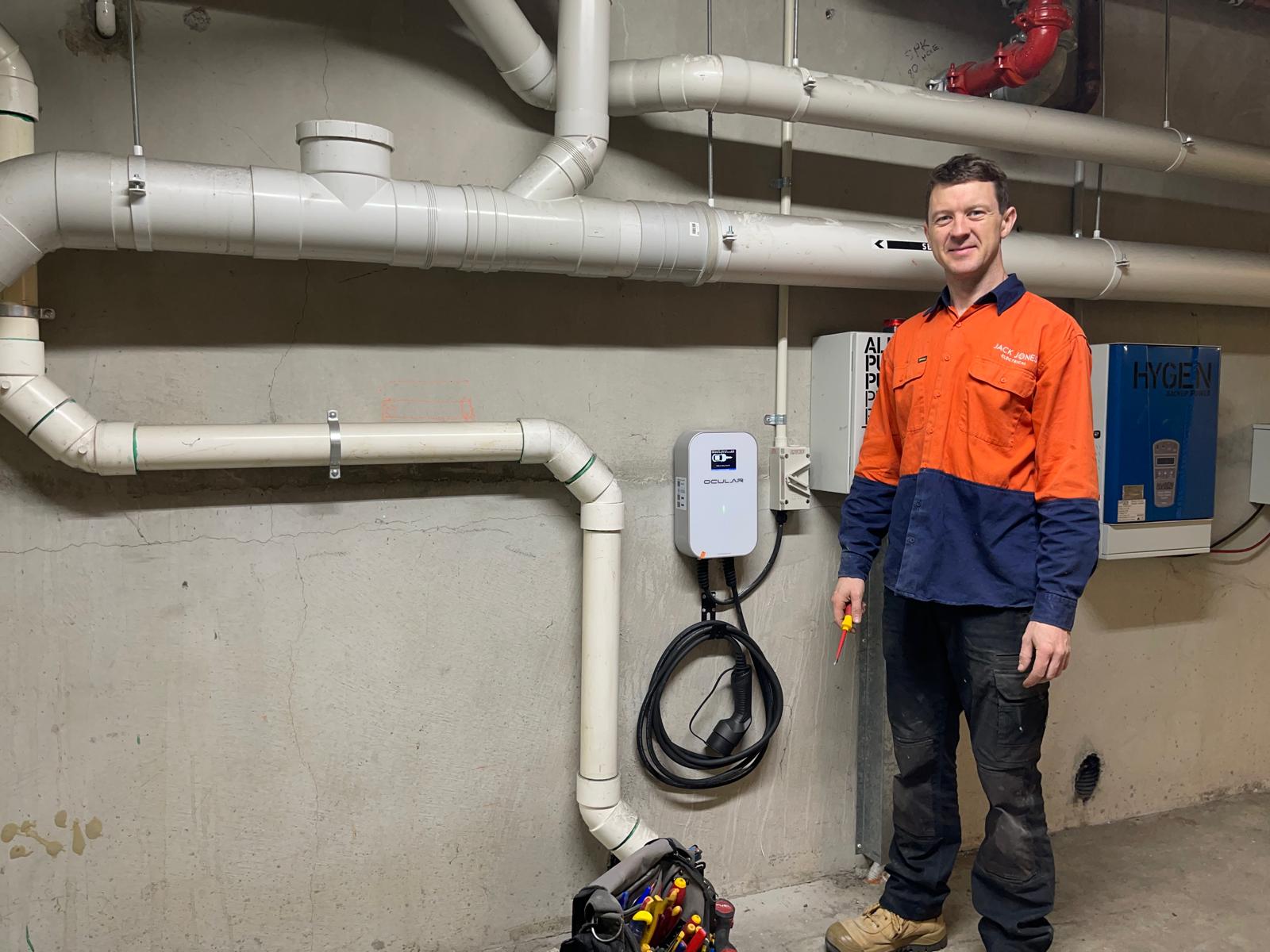 Jack Jones of Jack Jones Electrical beside an Ocular EV charger he installed on a basement wall